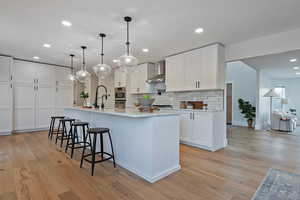 Kitchen with wall chimney range hood, white cabinets, and a spacious island