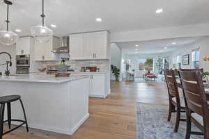 Kitchen with wall chimney exhaust hood, sink, white cabinetry, decorative light fixtures, and light wood-type flooring