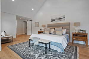 Bedroom with hardwood / wood-style flooring, a barn door, and high vaulted ceiling