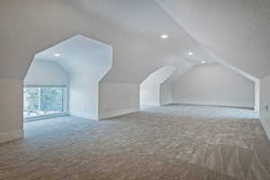 Bonus room featuring lofted ceiling, light carpet, and a textured ceiling