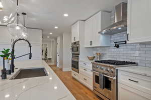 Kitchen featuring wall chimney range hood, sink, white cabinets, and appliances with stainless steel finishes