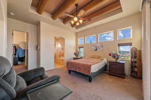 Carpeted bedroom with beamed ceiling, ensuite bathroom, a spacious closet, and a high ceiling