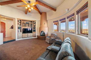 Living room with beam ceiling, a large fireplace, ceiling fan, and carpet