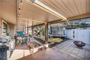 View of patio featuring a trampoline, a grill, and a fire pit