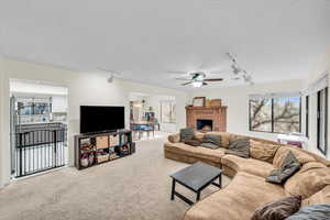 Living room featuring a brick fireplace, carpet floors, rail lighting, and a textured ceiling