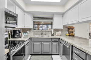 Kitchen featuring stainless steel appliances, sink, gray cabinetry, and a skylight