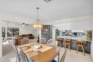 Dining space featuring ceiling fan with notable chandelier, track lighting, and light colored carpet