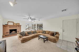 Living room with a brick fireplace, light carpet, a textured ceiling, and ceiling fan