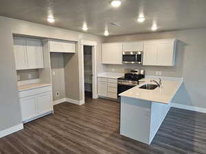 Kitchen with sink, dark wood-type flooring, appliances with stainless steel finishes, white cabinetry, and a textured ceiling