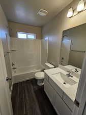 Full bathroom with shower / bathtub combination, hardwood / wood-style flooring, vanity, toilet, and a textured ceiling