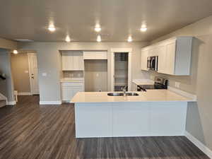 Kitchen with sink, dark hardwood / wood-style floors, kitchen peninsula, stainless steel appliances, and white cabinets