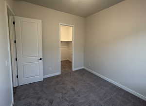 Unfurnished bedroom with a walk in closet, dark carpet, and a closet