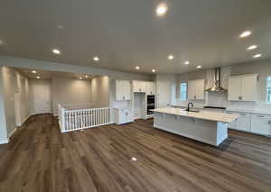 Kitchen with white cabinetry, gas cooktop, dark wood-type flooring, a center island with sink, and wall chimney exhaust hood