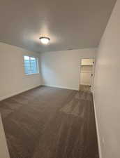 Unfurnished room featuring a textured ceiling and dark colored carpet