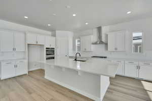 Kitchen featuring wall chimney range hood, sink, a kitchen island with sink, white cabinetry, and gas stovetop