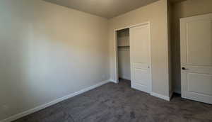 Unfurnished bedroom featuring dark carpet and a closet