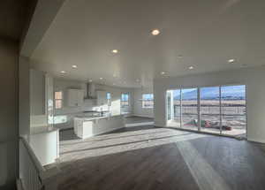 Kitchen with wall chimney exhaust hood, sink, light hardwood / wood-style flooring, a kitchen island, and white cabinets