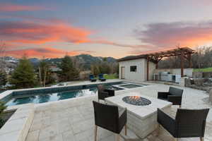 Pool at dusk featuring a patio area, a pergola, a mountain view, exterior kitchen, and a fire pit