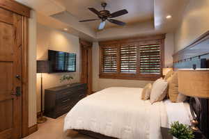 Bedroom with ceiling fan, light colored carpet, and a raised ceiling