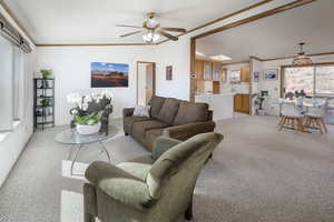 Living room featuring light carpet, vaulted ceiling, ornamental molding, and ceiling fan