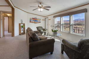 Living room with crown molding, a textured ceiling, ceiling fan, a mountain view, and light colored carpet