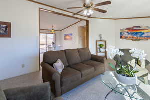 Carpeted living room with lofted ceiling, ornamental molding, and ceiling fan