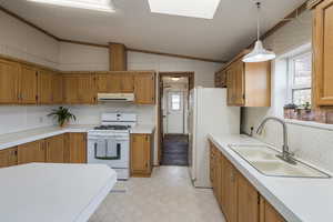 Kitchen featuring lofted ceiling with skylight, sink, hanging light fixtures, white appliances, and a textured ceiling