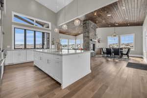 Kitchen featuring decorative light fixtures, sink, white cabinets, hardwood / wood-style flooring, and a kitchen island with sink