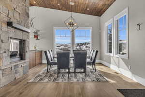 Dining space featuring a stone fireplace, an inviting chandelier, high vaulted ceiling, wood ceiling, and light wood-type flooring