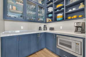 Bar with built in microwave, blue cabinets, light stone counters, and light wood-type flooring