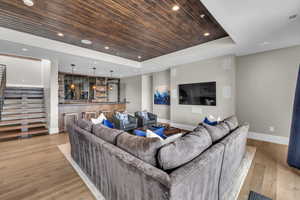 Living room with bar, a raised ceiling, light hardwood / wood-style floors, and wooden ceiling