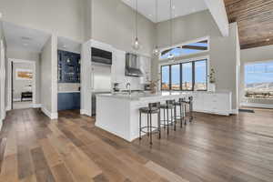 Kitchen featuring pendant lighting, a breakfast bar, wood-type flooring, white cabinets, and wall chimney exhaust hood