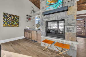 Bar with sink, a stone fireplace, light hardwood / wood-style floors, and a high ceiling