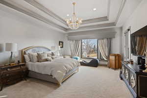 Bedroom with crown molding, light colored carpet, an inviting chandelier, and a tray ceiling