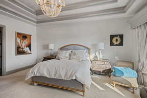 Bedroom with light colored carpet, ornamental molding, a tray ceiling, and a chandelier