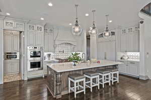 Kitchen featuring pendant lighting, dark wood-type flooring, premium range hood, stainless steel appliances, and an island with sink