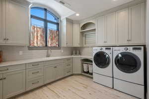 Washroom featuring cabinets, washing machine and clothes dryer, light hardwood / wood-style floors, and sink