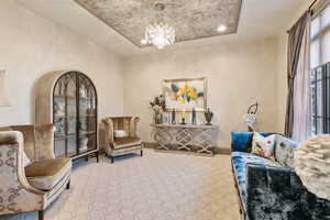 Living area featuring carpet flooring, a chandelier, and a raised ceiling