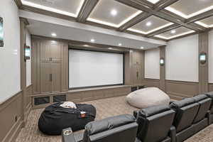 Carpeted home theater room featuring coffered ceiling, crown molding, and beamed ceiling