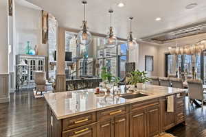 Kitchen featuring an island with sink, sink, light stone counters, and decorative light fixtures