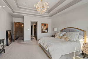 Carpeted bedroom with ensuite bath, a tray ceiling, and a chandelier