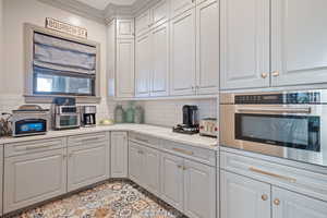 Kitchen featuring light stone counters, stainless steel oven, ornamental molding, and backsplash