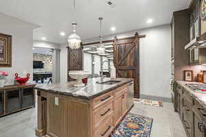 Kitchen featuring sink, appliances with stainless steel finishes, hanging light fixtures, a center island with sink, and a barn door