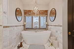 Bathroom with an inviting chandelier, a bath, and tile walls