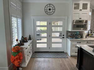 Doorway to outside with crown molding, a healthy amount of sunlight, sink, and light wood-type flooring