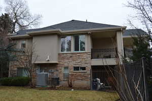 Rear view of property with central AC, a balcony, and a lawn