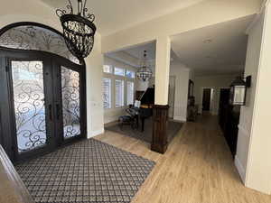 Foyer with crown molding, light wood-type flooring, an inviting chandelier, and french doors