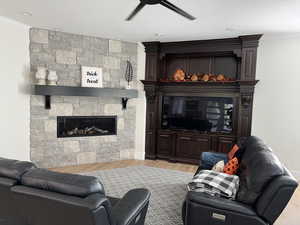 Living room with crown molding, a stone fireplace, a textured ceiling, and light hardwood / wood-style flooring