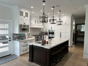 Kitchen featuring sink, hanging light fixtures, white cabinets, a center island with sink, and stainless steel double oven