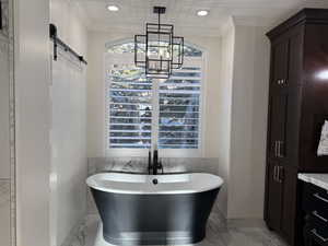 Bathroom featuring a notable chandelier, crown molding, a tub, and vanity